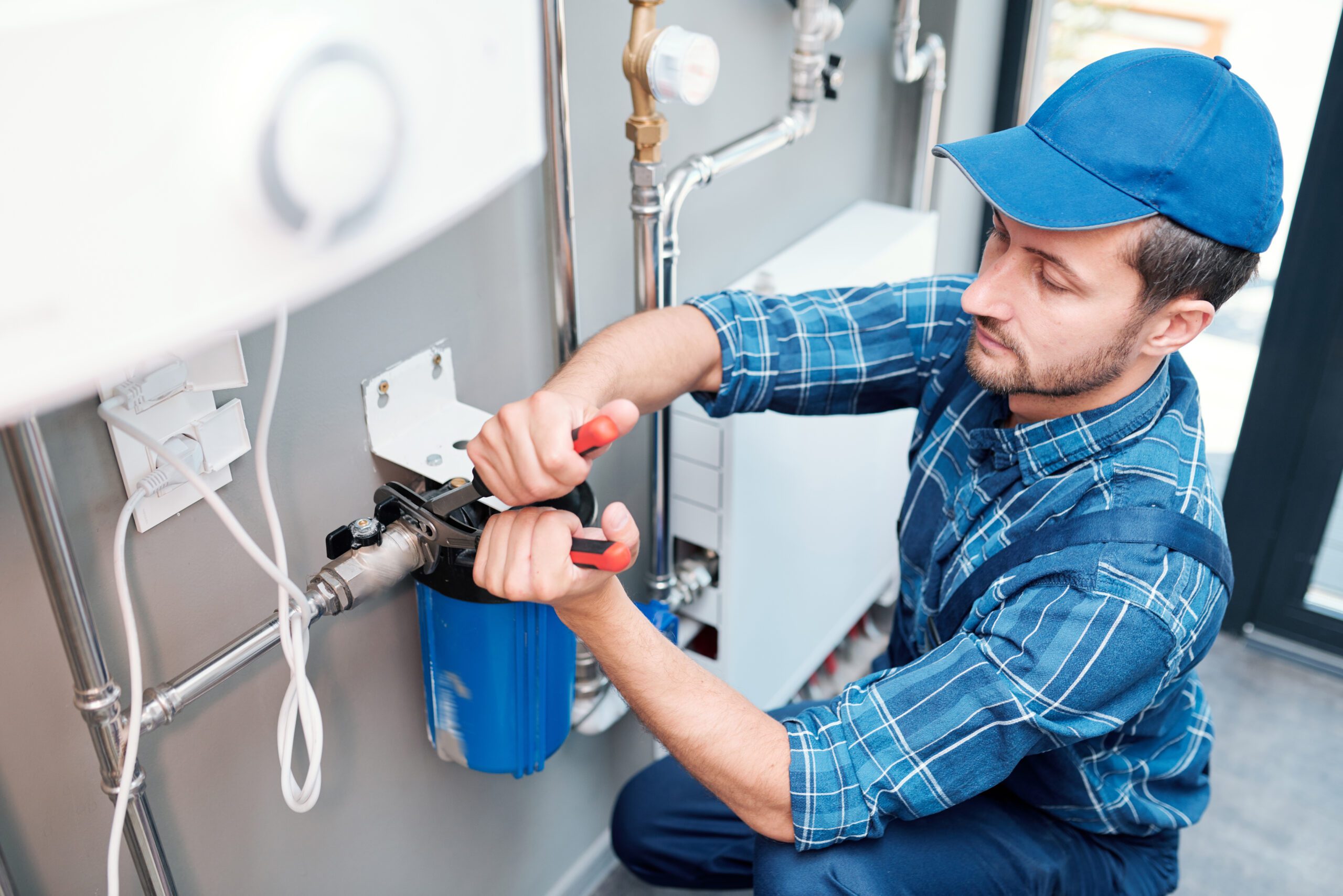 young man workwear using pliers while installing water filtration system kitchen client scaled